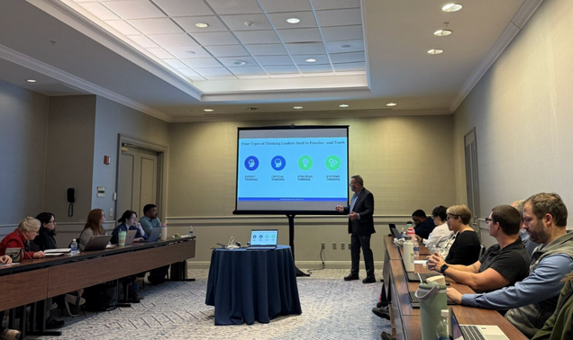 Man presenting a powerpoint in a conference room to learners sitting in a U-shape facing the screen.